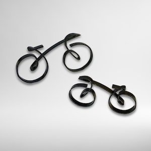 Peut inclure: Deux sculptures de vélos en métal noir. Les vélos sont faits de lignes métalliques courbes, avec un design minimaliste. Les roues et le cadre sont formés de lignes continues, créant une représentation artistique unique d'un vélo.