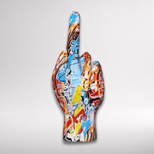 Puede incluir: Escultura de mano de cerámica con el dedo medio levantado, cubierta de graffiti colorido. La obra de arte presenta una mezcla de azules, naranjas, amarillos y rojos, con detalles en blanco y negro. Una pieza decorativa audaz.
