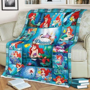 May include: A blue fleece blanket featuring a collage of images of a mermaid with red hair. The blanket has a turquoise border and includes the name "Dannii" in a central image. The mermaid is depicted in various underwater scenes.