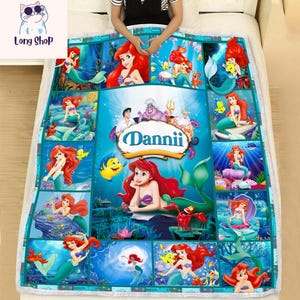 May include: A turquoise and white blanket featuring multiple images of a mermaid with red hair, surrounded by sea creatures. The blanket has the name "Dannii" in a banner. The blanket is on a white bed.