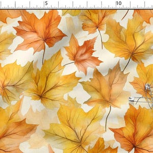 Pode incluir: Padrão de tecido com um padrão aquarela de folhas de bordo de outono em tons de amarelo, laranja e marrom. As folhas têm veias detalhadas e estão espalhadas sobre um fundo creme. Vários alfinetes de segurança prateados são visíveis.