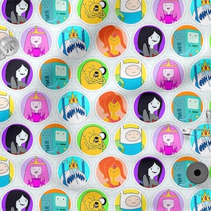 Könnte beinhalten: Weißer Stoff mit einem sich wiederholenden Muster aus kreisförmigen Bildern mit Charakteren aus Adventure Time. Die Kreise enthalten Finn, Jake, Prinzessin Bubblegum, Marceline und BMO. Sicherheitsnadeln und eine Garnrolle sind ebenfalls sichtbar.
