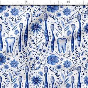 Op de afbeelding: Witte stof met een blauw bloemen- en tandheelkundig patroon. Het ontwerp bevat blauwe tandenborstels, tanden en diverse bloemen en bladeren. Het patroon wordt herhaald over de stof.