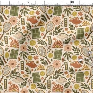 Könnte beinhalten: Ein Stoffmuster mit Tennisschlägern, gelben Tennisbällen, grünen Tennisplätzen, orangefarbenen Visieren und Blumenmotiven in Orange-, Gelb- und Grüntönen auf cremefarbenem Hintergrund, mit einer befestigten metallenen Sicherheitsnadel.