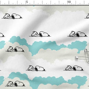 Peut inclure: Tissu blanc avec un motif répété de Snoopy dormant sur un nuage. Les nuages sont bleu clair et blancs. Les illustrations de Snoopy sont en noir et blanc.