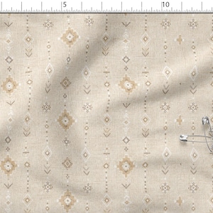 Puede incluir: Una tela de color beige con un patrón repetitivo de pequeñas formas geométricas blancas y tostadas, incluyendo diamantes y flechas, dispuestas en columnas verticales. Una regla metálica de 15 cm es visible en el borde superior, con tres imperdibles.