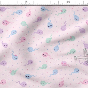 Könnte beinhalten: Ein hellrosa Stoff mit einem sich wiederholenden Muster aus kleinen, cartoonartigen Spermienfiguren in Pastellblau, Grün, Lila und Pink, akzentuiert mit winzigen Sternen und Punkten, abgebildet neben einem 15 cm Lineal und mehreren silbernen Sicherheitsnadeln.