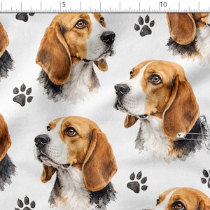 Può includere: Un tessuto bianco con un motivo ripetuto ad acquerello di teste di cane beagle e impronte di zampe nere. Il tessuto è posizionato accanto a un righello con scala in centimetri, con le teste di beagle che misurano circa 7,5 cm di larghezza.