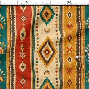 Puede incluir: Una tela con un patrón de rayas verticales en azul verdoso, naranja óxido y amarillo mostaza, con motivos geométricos de diamantes y soles. Una regla metálica en la parte superior marca 15 cm y un imperdible está sujeto a la tela.