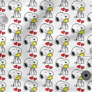 Peut inclure: Tissu blanc avec un motif répété de Snoopy et Woodstock se câlinant, avec des cœurs rouges. Les personnages de dessins animés sont en contour noir avec des accents jaunes et blancs. Épingles et une punaise noire visibles.