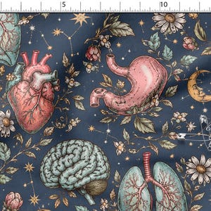 Könnte beinhalten: Ein dunkelblauer Stoff mit einem sich wiederholenden Muster aus anatomischen Illustrationen, darunter Herzen, Mägen, Gehirne und Lungen, durchsetzt mit Gänseblümchen, Blättern, Sternen und einer Mondsichel. Eine Sicherheitsnadel ist am Stoff befestigt.