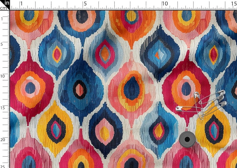 May include: Colorful fabric with a repeating pattern of teardrop shapes in shades of blue, orange, pink, and yellow. The fabric has a textured appearance. Safety pins and a spool of thread are on the fabric.