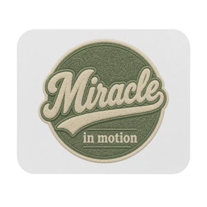 Op de afbeelding: Een ronde geborduurde patch met een getextureerde saliegroene achtergrond en een crèmekleurige rand. Het woord Miracle is geborduurd in een groot, crèmekleurig cursief lettertype met een streep eronder, en de tekst in motion staat daaronder.