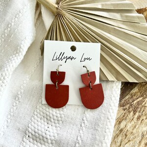 May include: A pair of red leather earrings with a geometric design. The earrings are on a white card with the text "Lilly Lou" written on it.