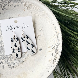 May include: White and black cork earrings with a tree pattern. The earrings are rectangular with rounded edges and hang from silver hooks. The earrings are displayed on a white card with the text "Lillyan Lou".