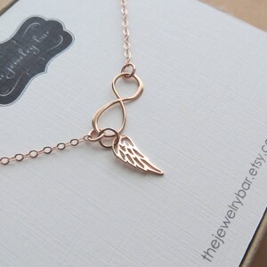 Pu&ograve; includere: Collana infinita in oro rosa con un delicato ciondolo ad ala d'angelo. La collana &egrave; su uno sfondo bianco con il testo "thejewelrybar.etsy.com".