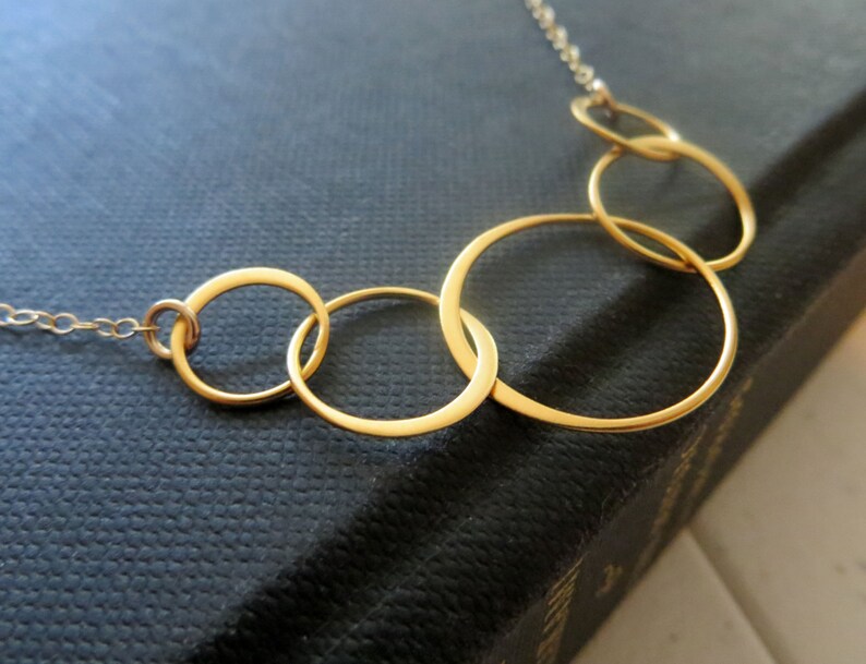 May include: A gold necklace with five interlocking circles of varying sizes.