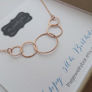 May include: A rose gold necklace with five interlocking circles. The necklace is displayed on a white card with the text "Happy 50th Birthday! thejewelrybar.etsy.com"