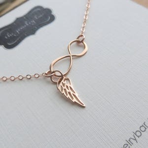 Pu&ograve; includere: Una collana a infinito in oro rosa con un delicato ciondolo ad ala d'angelo. La collana &egrave; su uno sfondo bianco.