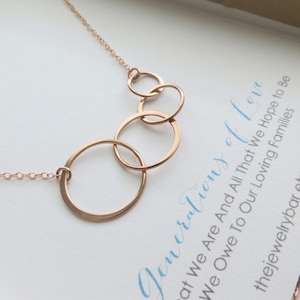 Puede incluir: Un collar de oro rosa con cuatro círculos interconectados de diferentes tamaños. Los círculos están conectados en una disposición en cascada, suspendidos de una fina cadena. El fondo incluye el texto "Generations of Love".