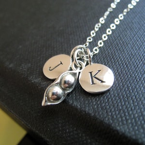 May include: A silver necklace with a pea pod charm and two initial charms. The initial charms are 'J' and 'K'.