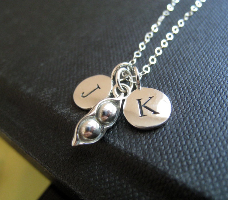 May include: A silver necklace with a pea pod charm and two initial charms. The initial charms are 'J' and 'K'.