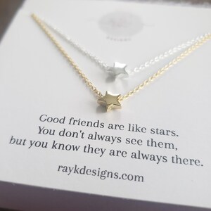 May include: Two delicate star necklaces, one gold and one silver, are displayed on a white card. The gold necklace is in the foreground, with a small star pendant. The card has text that reads, "Good friends are like stars..." and the website raykdesigns.com.