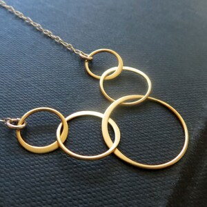 May include: A gold necklace with five interlocking circles of varying sizes. The necklace is on a black background.