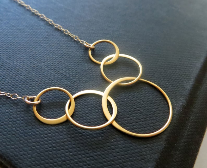 May include: A gold necklace with five interlocking circles of varying sizes. The necklace is on a black background.