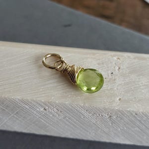 May include: A gold wire wrapped pendant featuring a light green gemstone.
