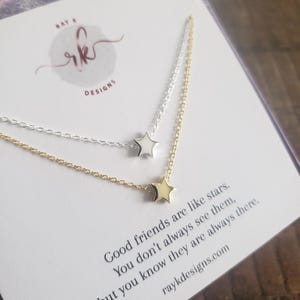 May include: Two delicate star necklaces, one silver and one gold, are displayed on a card with the text "Good friends are like stars." The necklaces feature small star pendants and fine chains. The card also includes the text "raykdesigns.com".