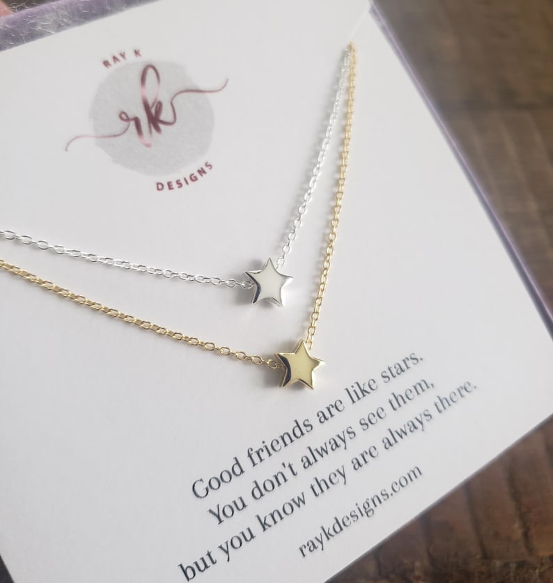 May include: Two delicate star necklaces, one silver and one gold, are displayed on a card with the text "Good friends are like stars." The necklaces feature small star pendants and fine chains. The card also includes the text "raykdesigns.com".