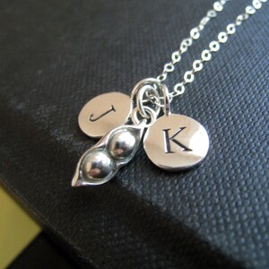 May include: Silver necklace with a pea pod charm and two initial charms. The initials are "J" and "K".