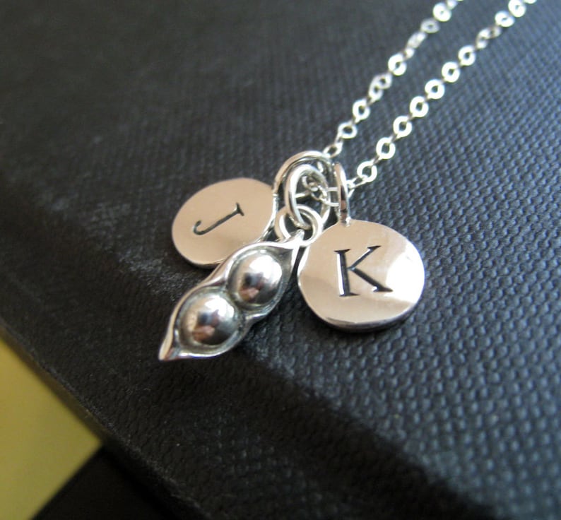 May include: Silver necklace with a pea pod charm and two initial charms. The initials are "J" and "K".