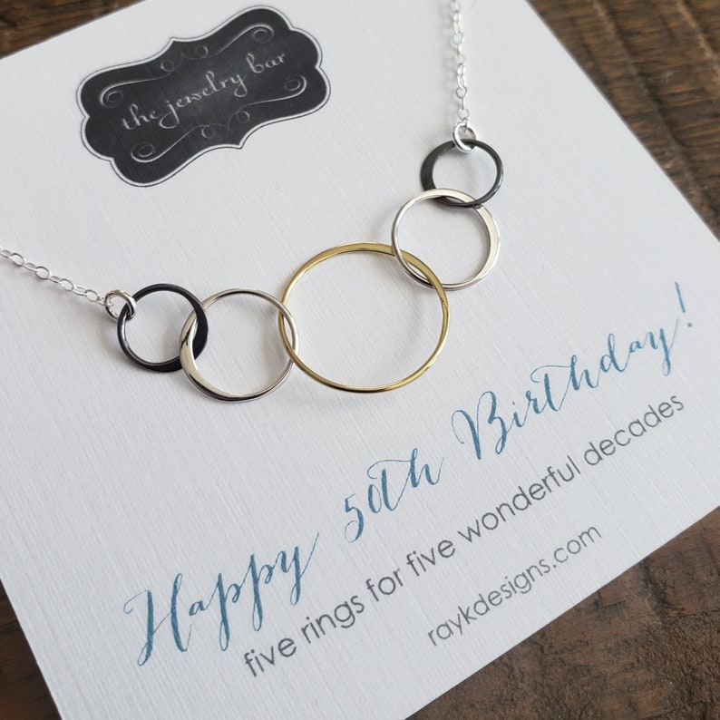 May include: A silver necklace with five interlocking rings, one gold ring, and the text "Happy 50th Birthday! five rings for five wonderful decades raykdesigns.com".