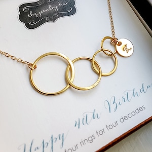 May include: Gold necklace with four interlocking circles and a small charm with the letter K. The necklace is in a box with the text "Happy 40th Birthday four rings for four decades".