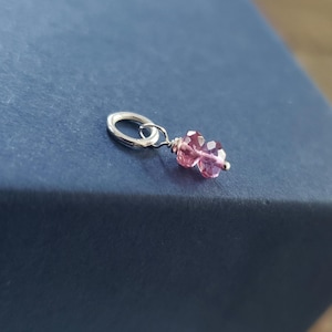 May include: A silver charm with a pink crystal bead. The charm is in the shape of a circle with a small loop at the top.