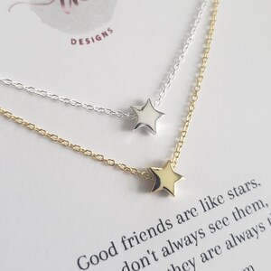 May include: Two delicate star necklaces, one silver and one gold, are displayed on a white card. The card features the text "Good friends are like stars" and the website raykdesigns.com. The necklaces are a simple, elegant design.