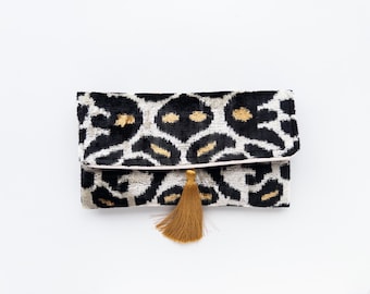 Puede incluir: Clutch negra y blanca con un borla dorada. La clutch tiene un patrón geométrico y está hecha de terciopelo.