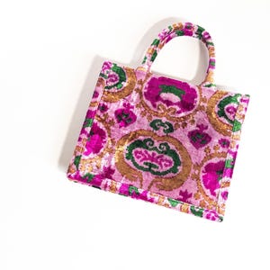 May include: A pink and green patterned tote bag with a velvet texture. The bag has a top handle and a rectangular shape.