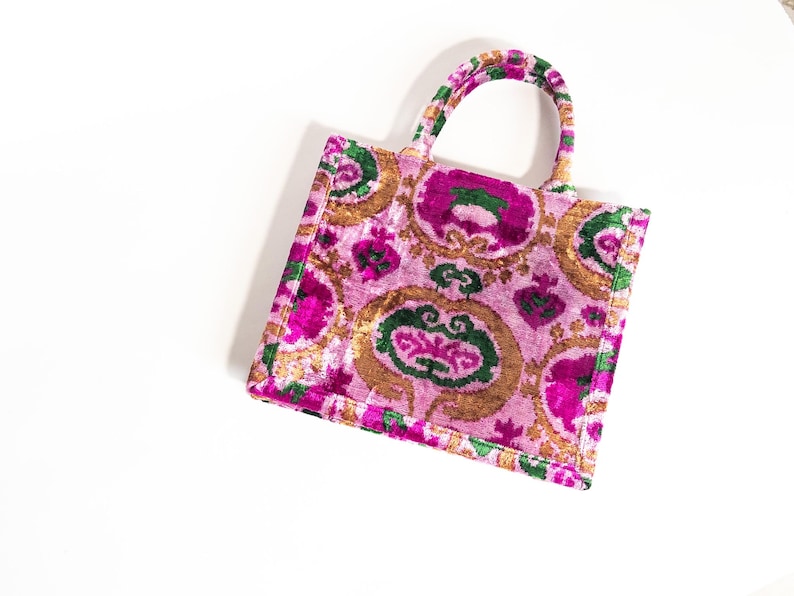 May include: A pink and green patterned tote bag with a velvet texture. The bag has a top handle and a rectangular shape.