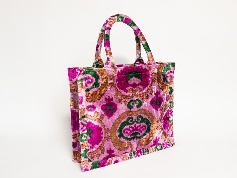 May include: A pink, gold, and green floral tote bag with a velvet texture. The bag has two top handles.