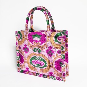 May include: A pink, green, and gold tote bag with a floral pattern. The bag has two handles and a zipper closure.