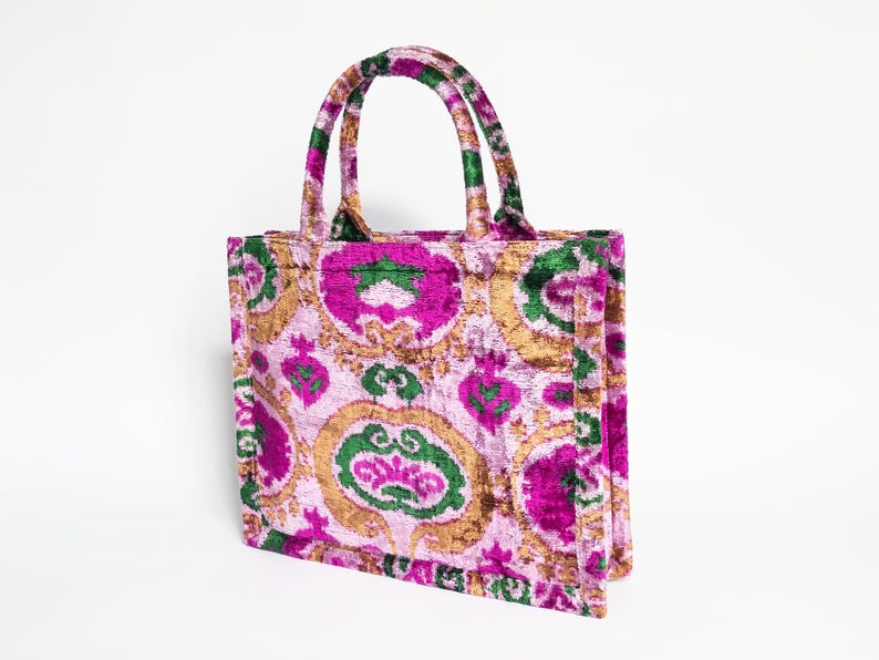May include: A pink, green, and gold tote bag with a floral pattern. The bag has two handles and a zipper closure.