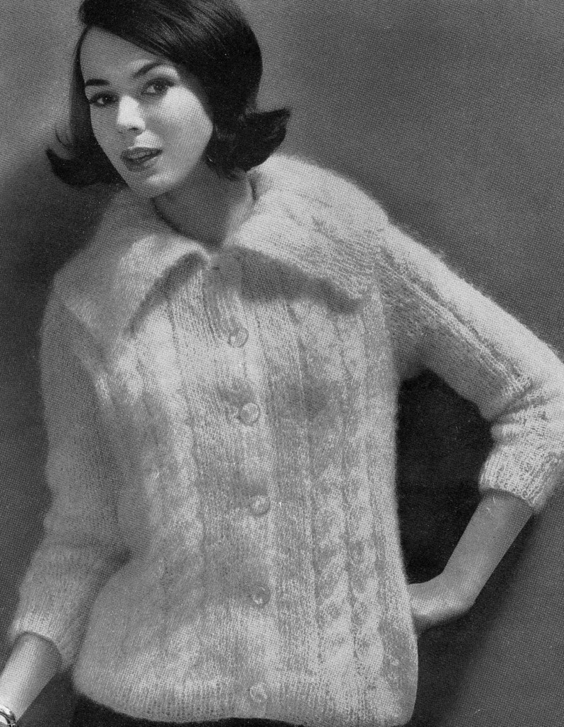 May include: A white knitted cardigan with a large collar and button closure. The cardigan has a cable knit pattern and is worn by a woman with short dark hair.