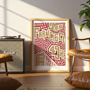 May include: A framed art print with the words "SAN FRANCISCO 49ERS" in gold and red. The print is leaning against a wall next to a Marshall speaker and a leather armchair. A record player sits atop the speaker.