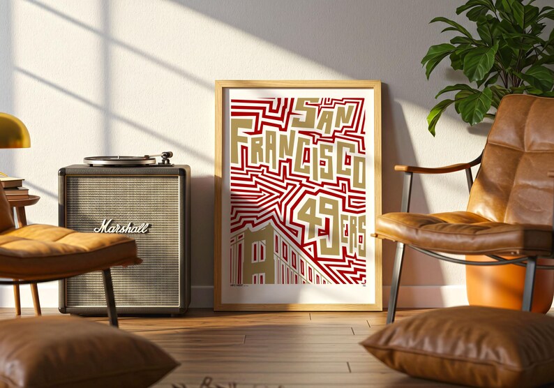 May include: A framed art print with the words "SAN FRANCISCO 49ERS" in gold and red. The print is leaning against a wall next to a Marshall speaker and a leather armchair. A record player sits atop the speaker.