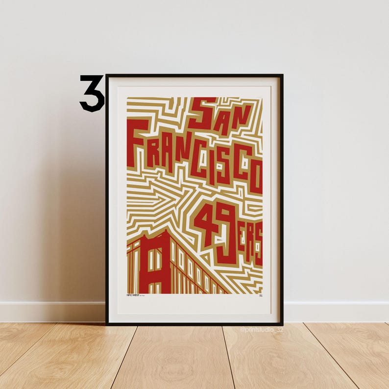 May include: Framed art print with the words "SAN FRANCISCO 49ERS" in red, set against a gold and white background. The print includes a building illustration. The artwork is presented in a black frame.