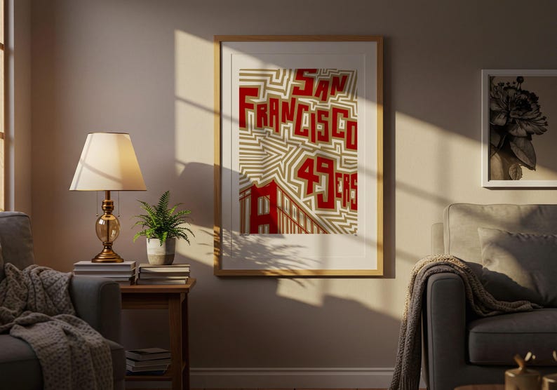 May include: A framed print with the words "San Francisco 49ers" in red block letters on a beige and white geometric design. The print is in a room with a lamp and a small potted plant.