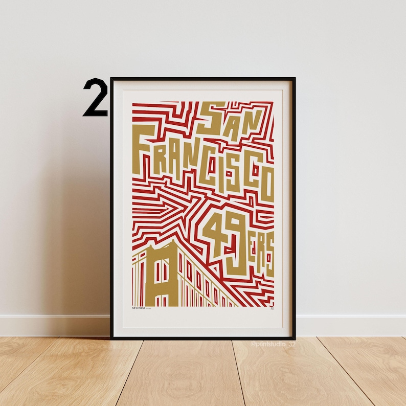 May include: Framed art print with the text "SAN FRANCISCO 49ERS" in gold, set against a red and white geometric pattern. The artwork includes a stylized building illustration. The print is presented in a black frame.